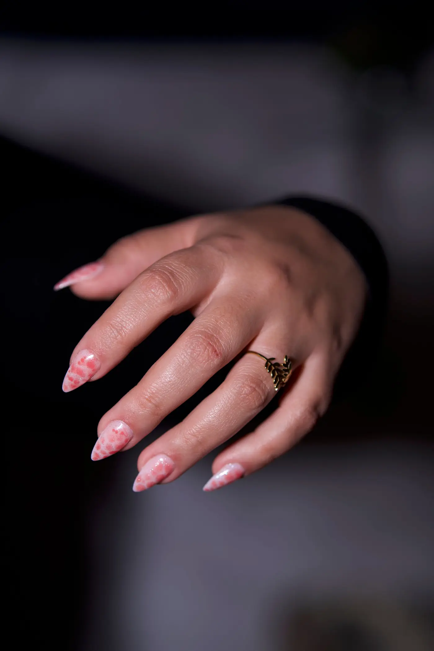 Close-up of a manicured hand with soft pink nails and a gold ring